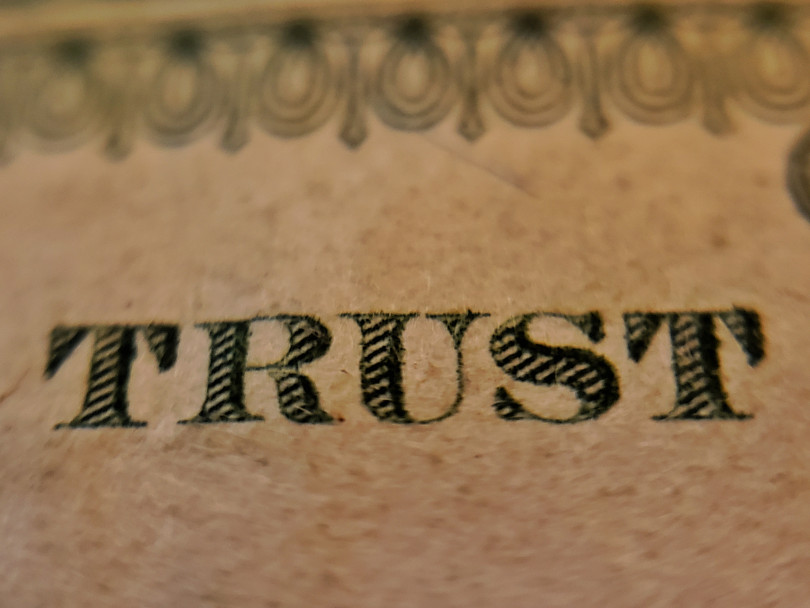 Picture of a american bank note, focus on the "Trust" part of the writing "In god we trust"