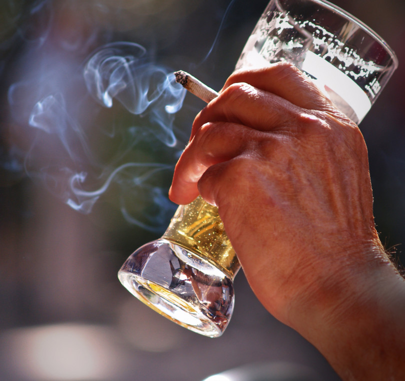 Man's hand holding a cigarette and a glass of beer.