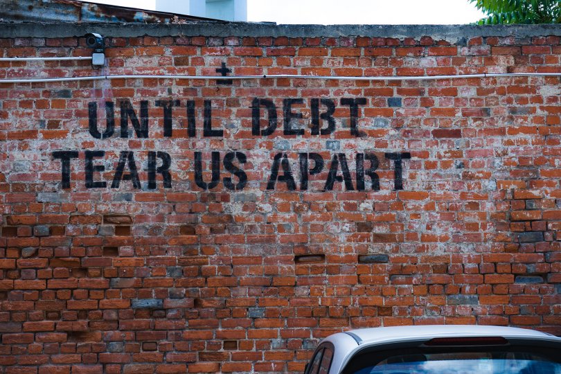 Photo d'un mur avec un tag disant "Until debt tear us apart"