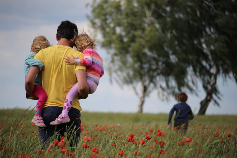 scène de famille dans une prairie, le père tenant deux de ses enfants dans ses bras 