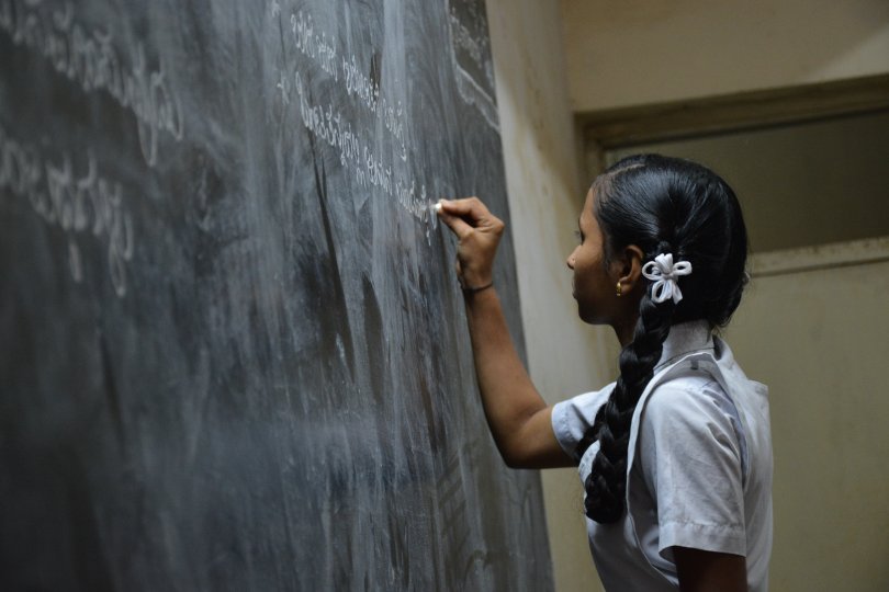 Jeune fille d'origine indienne en train d'écrire devant un tableau noir d'école