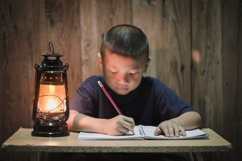 young central asian boy working lit by a lantern