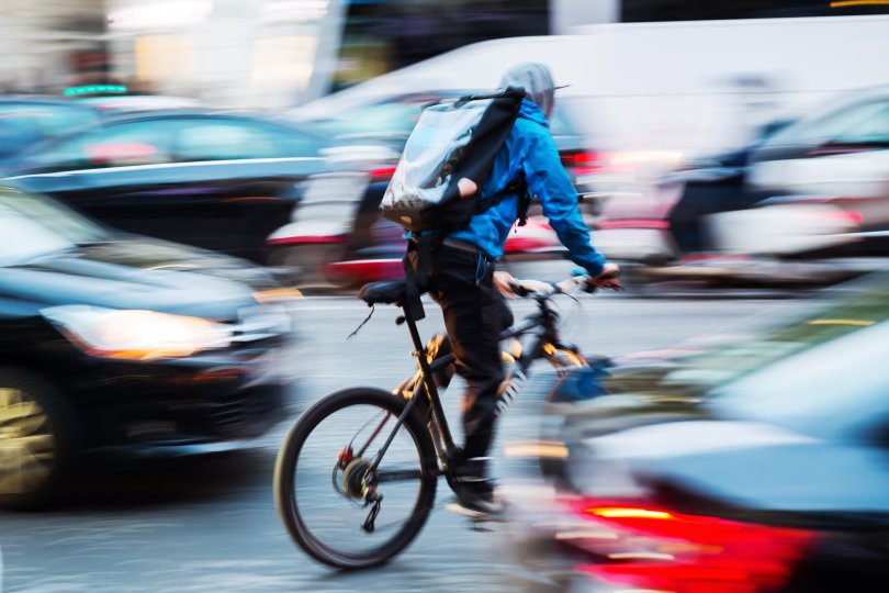 Livreur à vélo slalomant entre des voitures