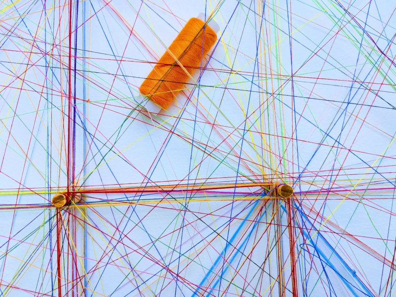 Ensemble de fil de couleurs formant des réseaux avec des épingles pour illustrer des nœuds d'interactions.