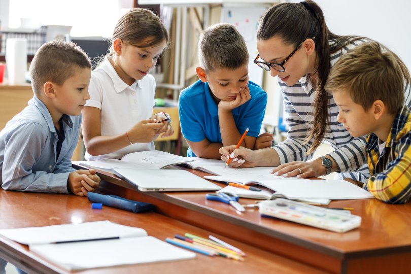 group of children around a teacher explaining a point.